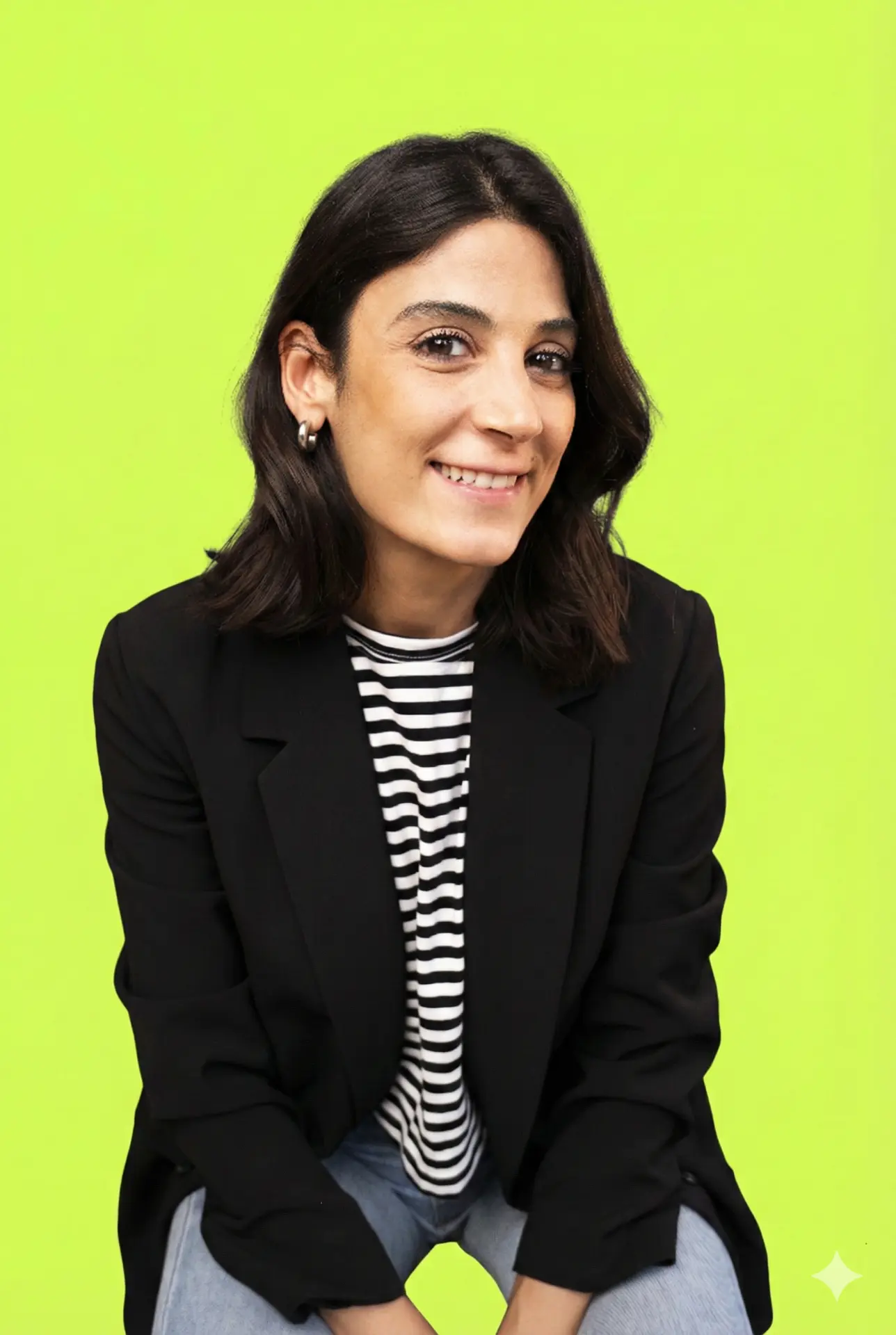 Portrait of Jules, technology founder, smiling in a black blazer and striped top against a bright green background